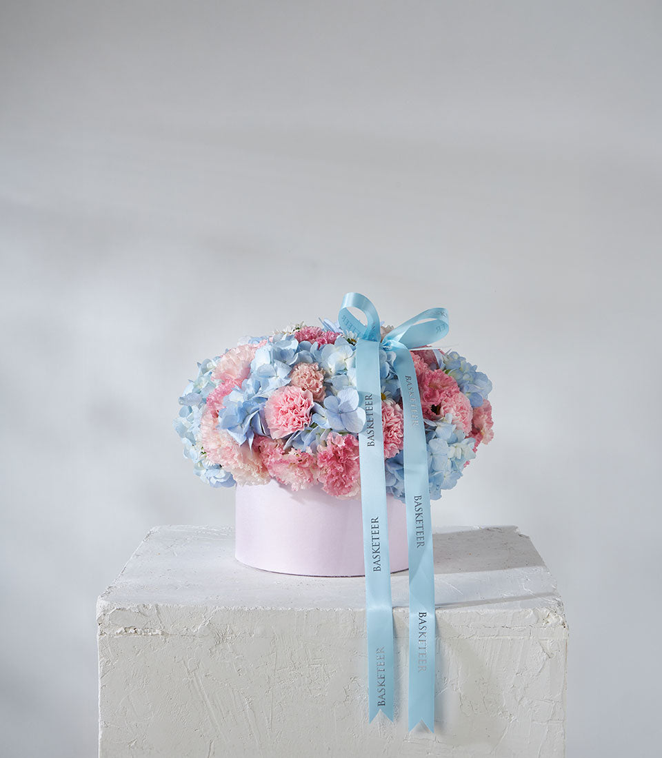 Blue hydrangeas and pink carnations in pastel hatbox with satin ribbon
