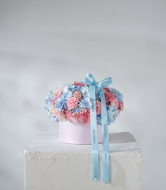 Blue hydrangeas and pink carnations in pastel hatbox with satin ribbon
