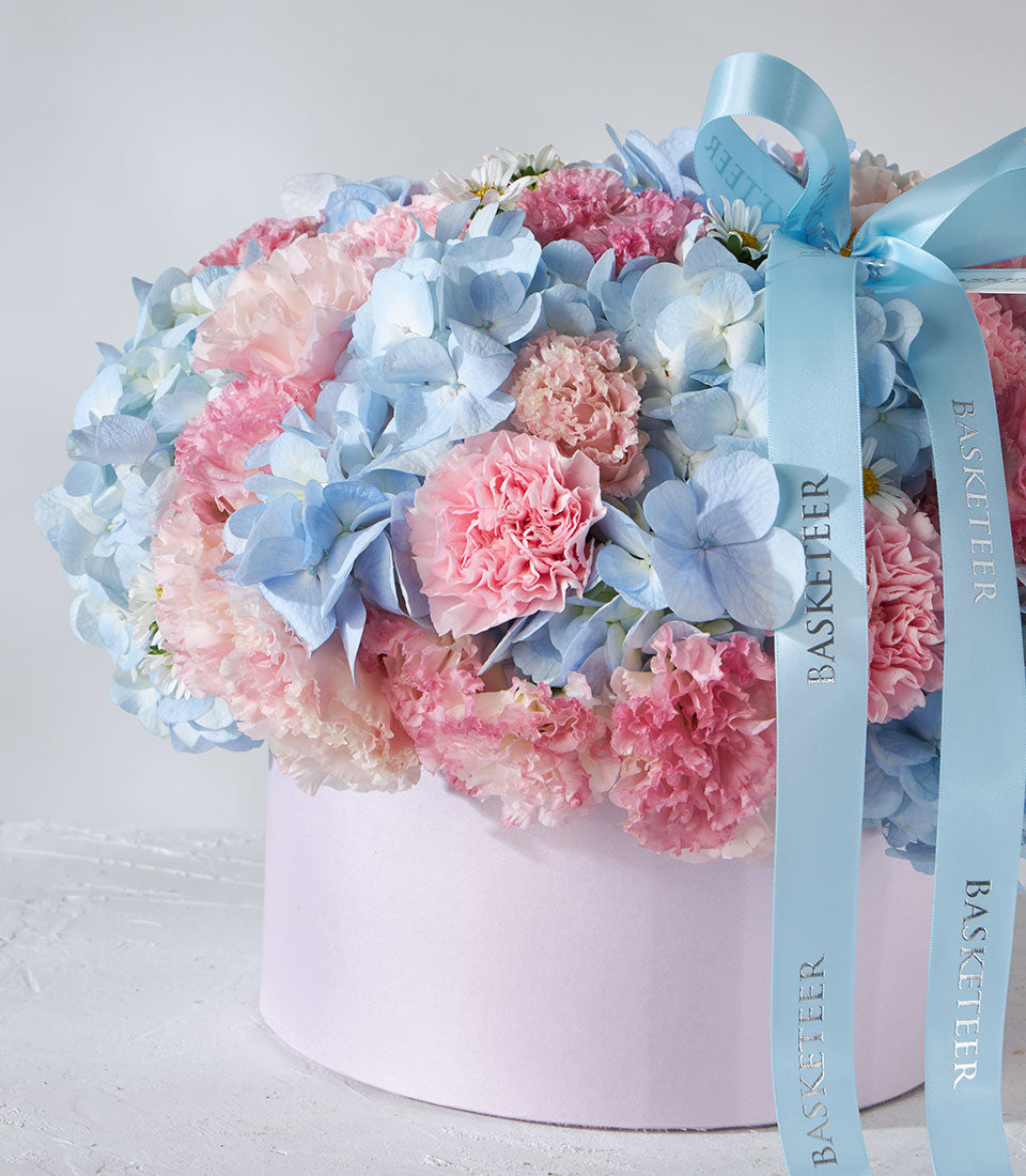 Pastel blue hydrangeas and pink carnations in light pink hatbox with satin ribbon