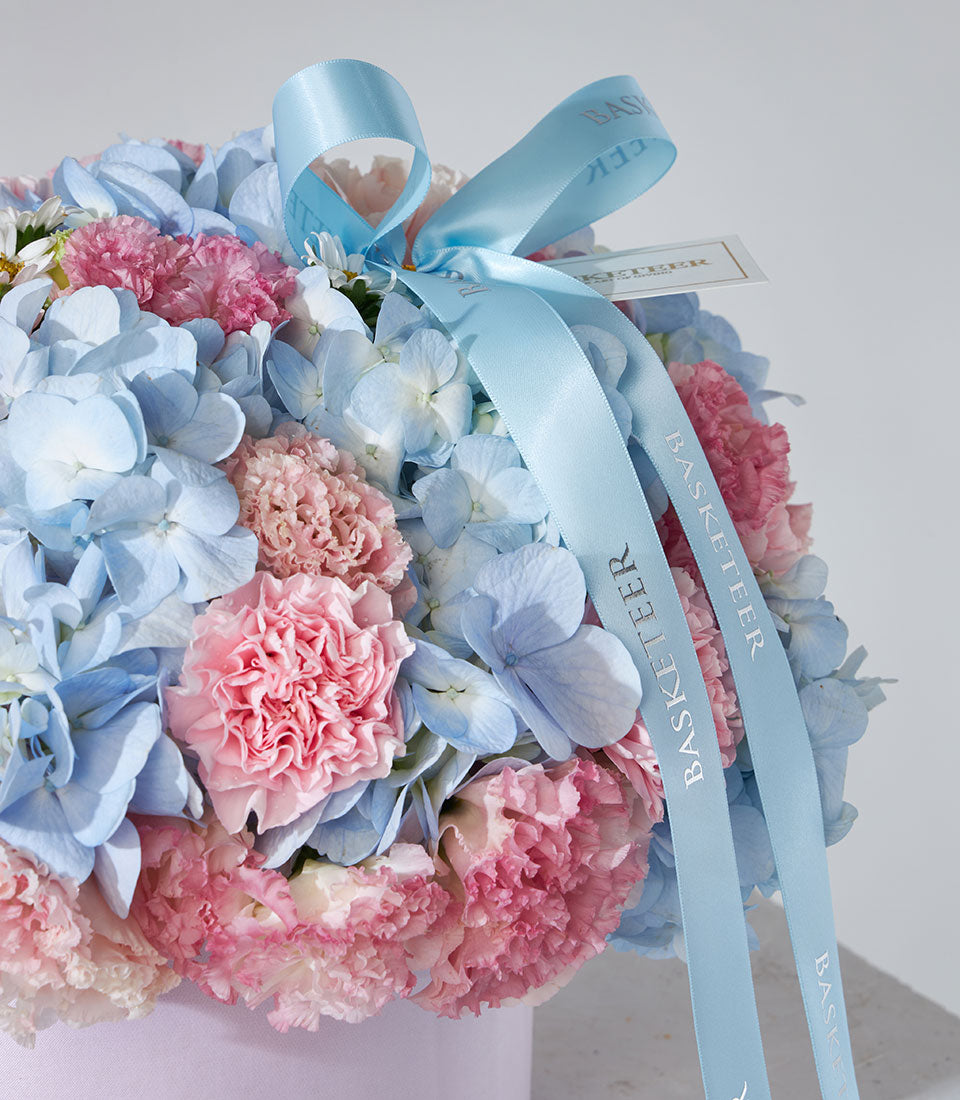 Pastel blue hydrangeas and pink carnations in light purple gift box with satin ribbon
