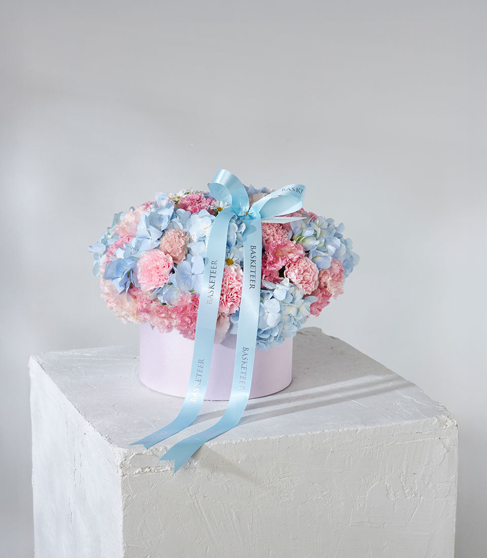 Pastel blue hydrangeas and pink carnations in luxury hatbox with satin ribbon