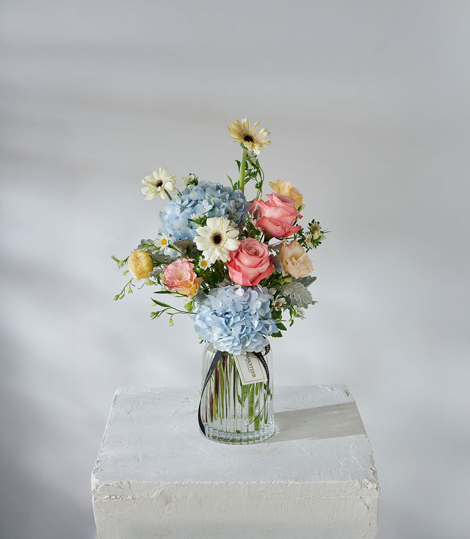 Kahara roses and blue hydrangeas in clear ribbed glass vase with ribbon
