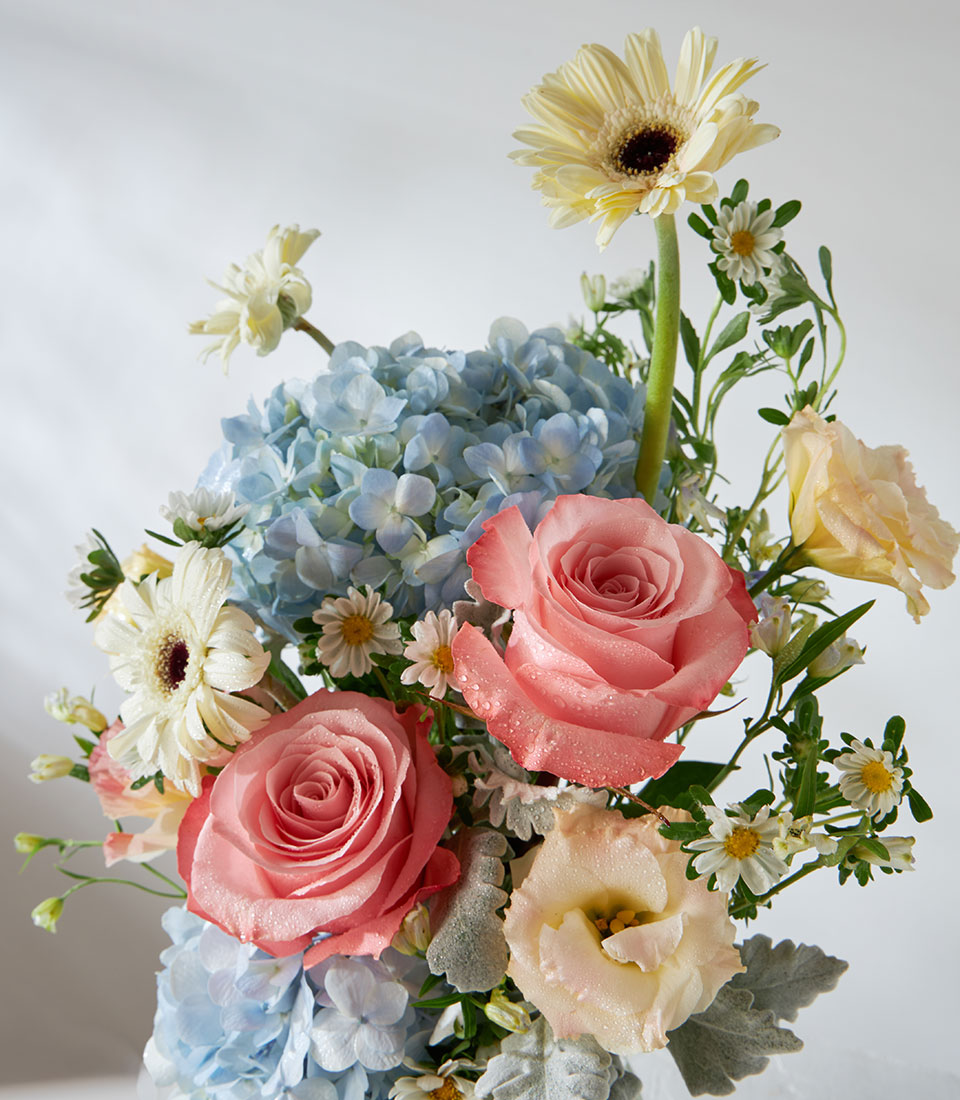 Kahara roses and blue hydrangeas in clear glass vase with gerbera daisy and lisianthus