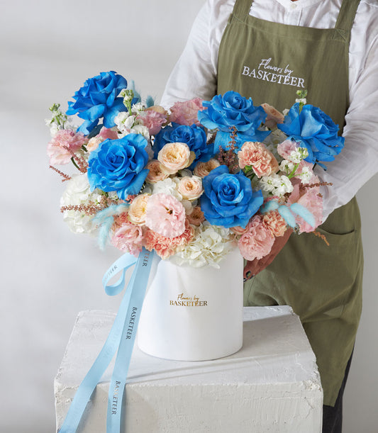 Florist holding premium blue rose and pastel garden rose arrangement in white box with blue ribbon