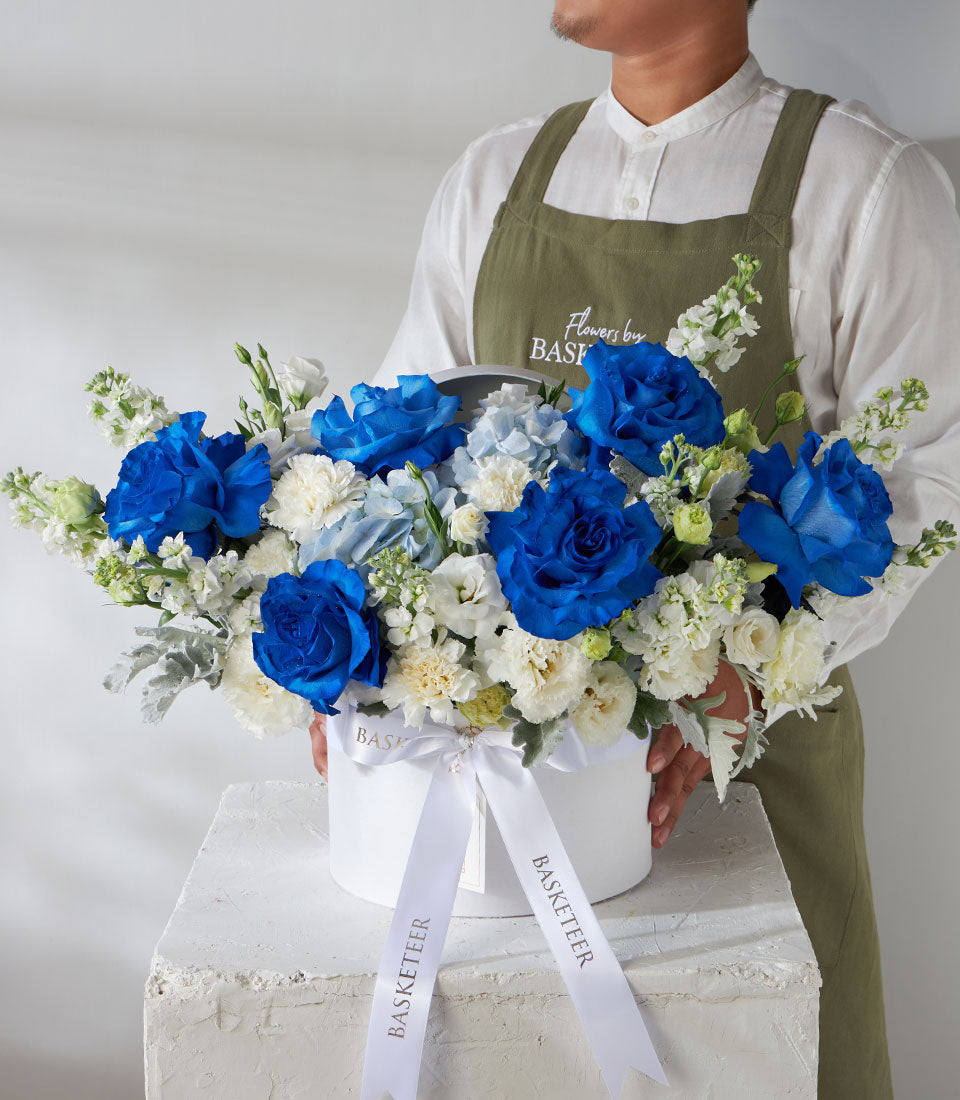 Tinted blue roses and white carnations in elegant round flower box with satin ribbon