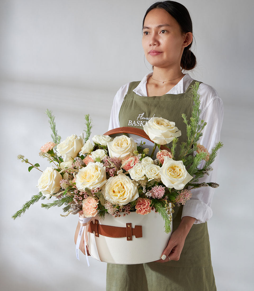 Cream roses and peach carnations in white leather flower box with brown straps