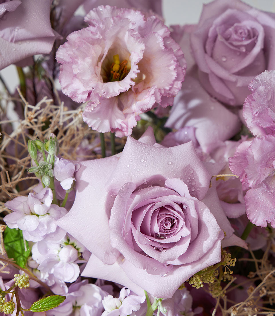 Purple and pink roses with lavender hydrangea and lisianthus in a fresh floral basket arrangement