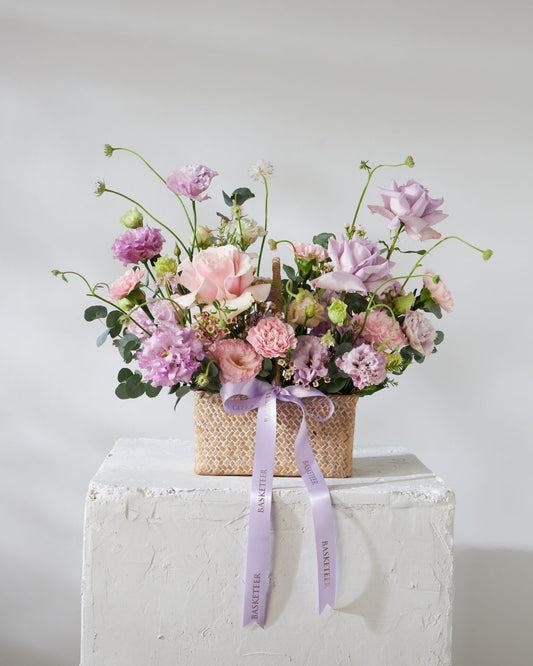 Fresh pink and purple roses in woven basket with purple ribbon, get well flowers