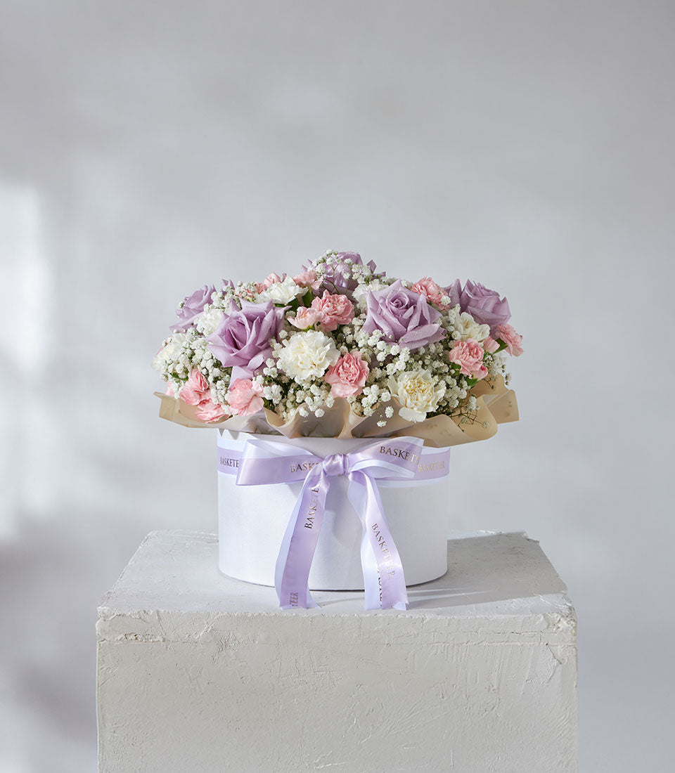 Lavender roses and pastel carnations arranged in white hatbox with satin ribbon