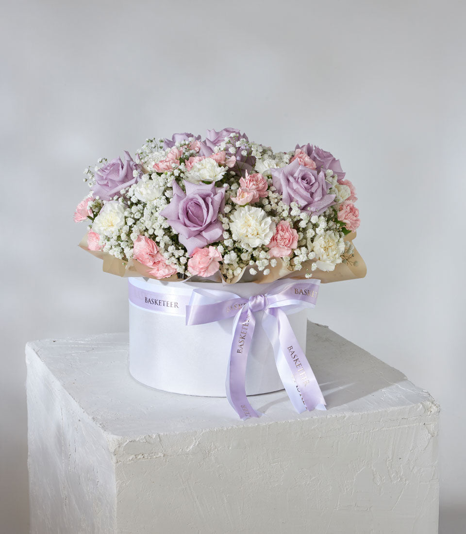 Lavender roses and pastel carnations in white hatbox with purple ribbon