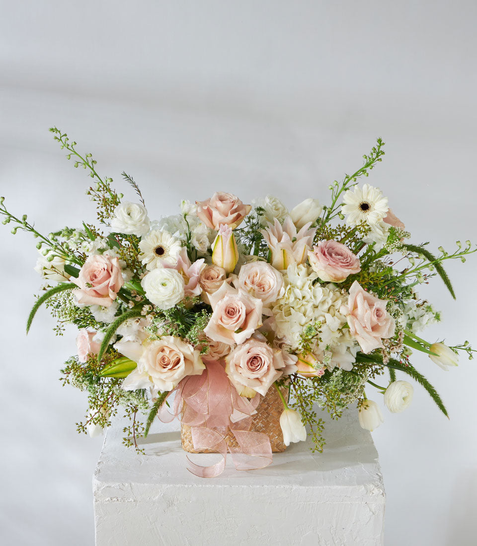 Luxe woven basket with quicksand roses, white lilies, hydrangeas and ranunculus in soft pastels
