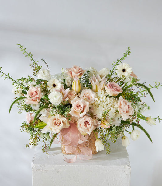 Luxe woven basket with quicksand roses, white lilies, hydrangeas and ranunculus in soft pastels