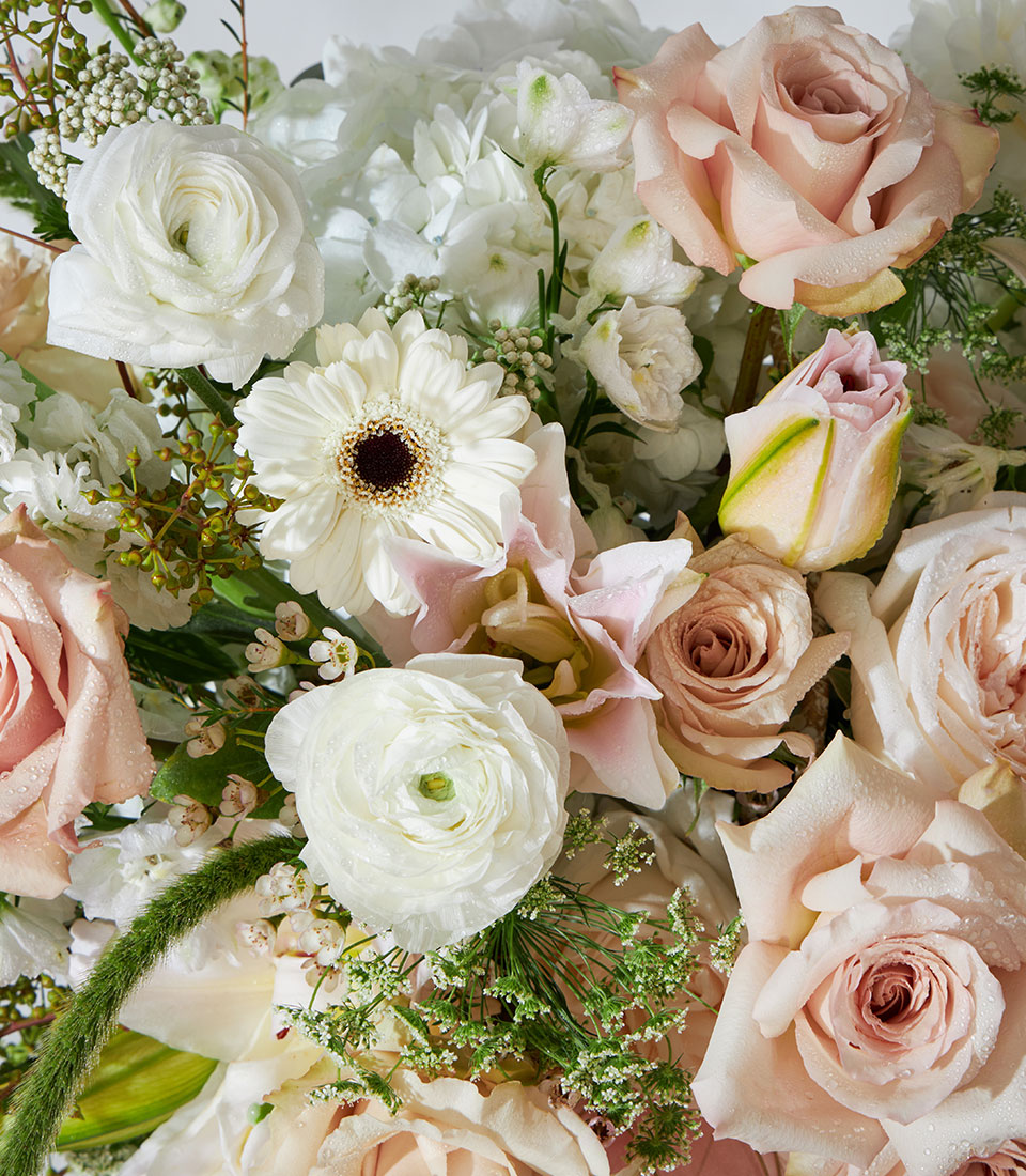 Luxury floral basket with quicksand roses, white lilies, ranunculus, and fresh foliage in soft pink and cream tones