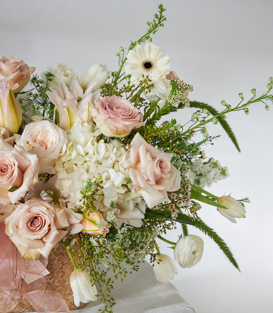 Luxury floral basket with quicksand roses, white lilies, hydrangeas, and ranunculus in woven container