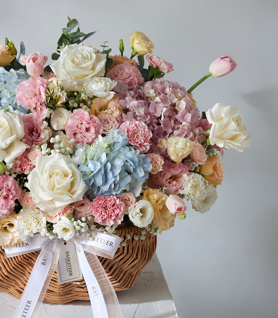 Pastel flower basket with roses, hydrangeas, and carnations in soft pink, blue, and cream tones