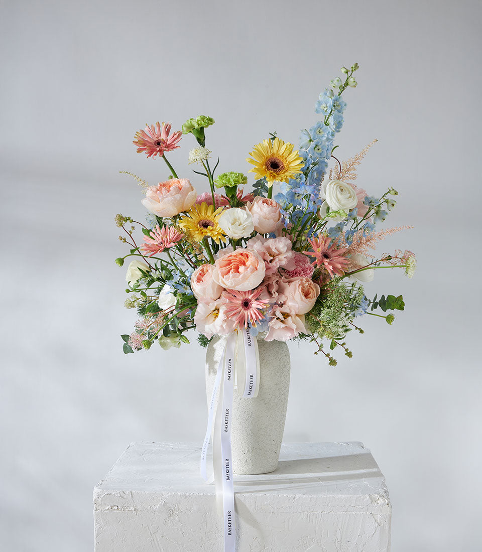 Juliet roses and pastel garden flowers in ceramic vase with pink, peach, yellow, and blue blooms
