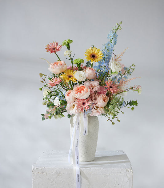 Juliet roses and pastel garden flowers in ceramic vase with pink, peach, yellow, and blue blooms