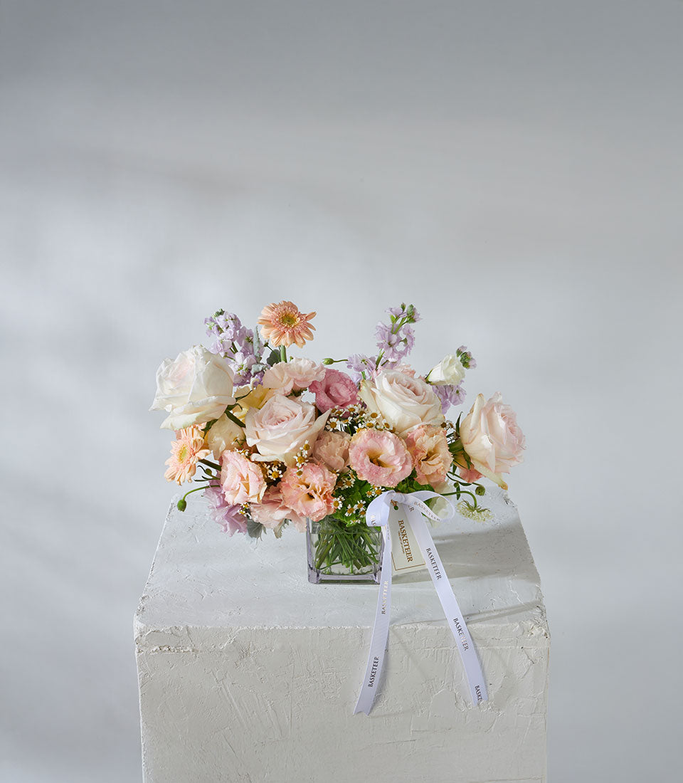 White O'Hara roses and peach garden flowers in square glass vase with ribbon