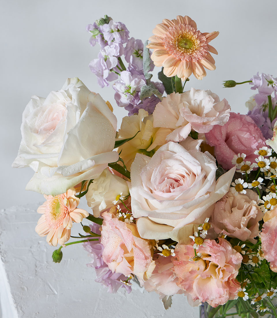 White O'Hara roses and peach garden flowers in square glass vase with purple stock