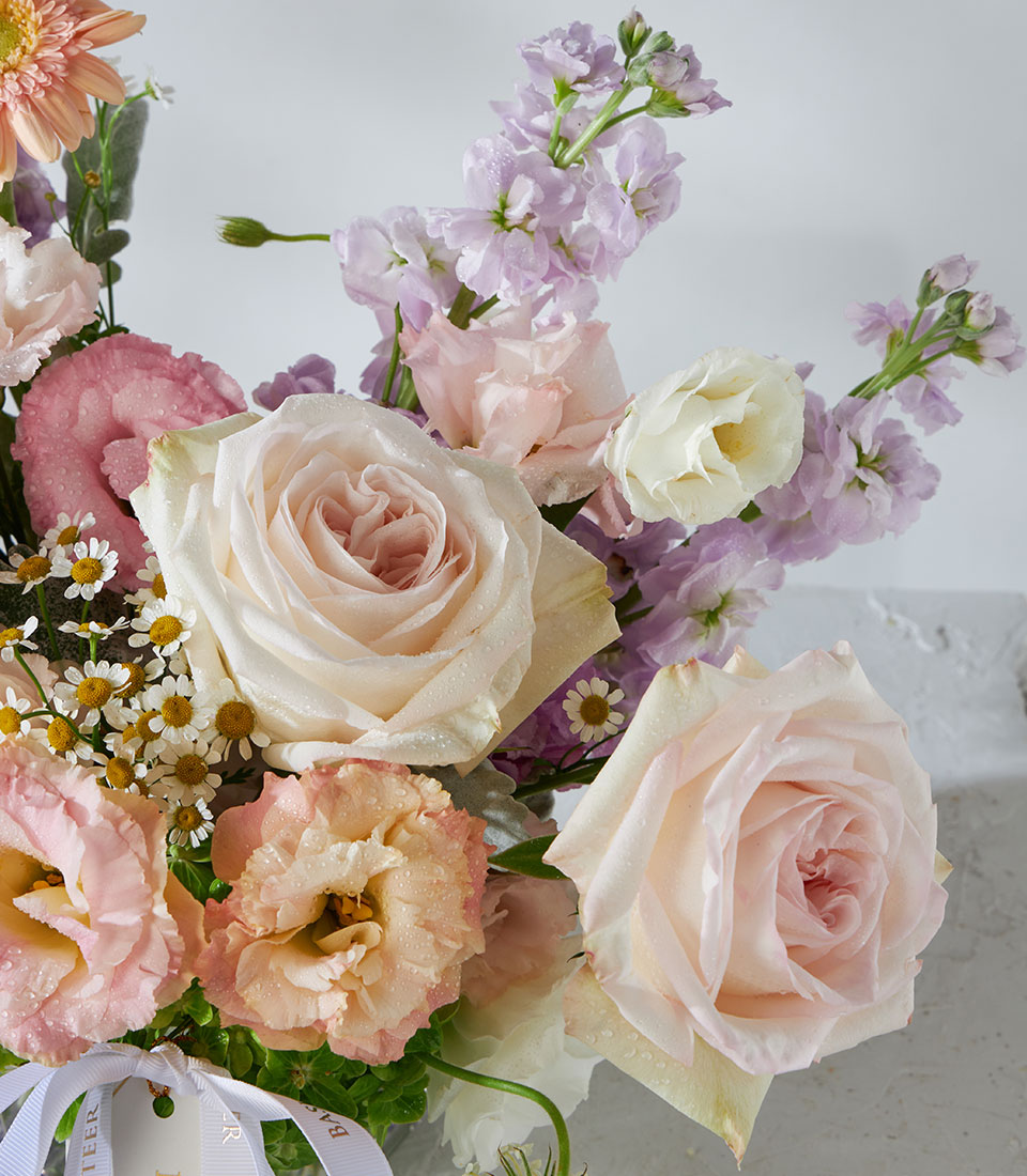 White O'Hara roses and peach garden flowers with chamomile and stock in square glass vase
