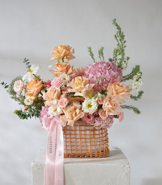 Peach roses and pink hydrangea arrangement in woven wicker basket with eucalyptus
