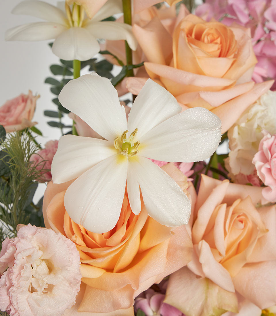 Peach roses and pink hydrangea in a soft woven basket with green foliage