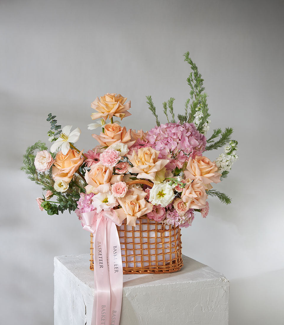 Peach roses and pink hydrangea arrangement in woven wicker basket with satin ribbons
