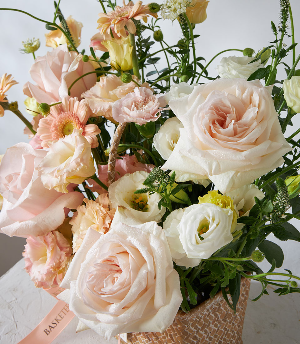 Pastel white and pink roses in woven basket with gerbera daisies and lisianthus for birthday celebrations