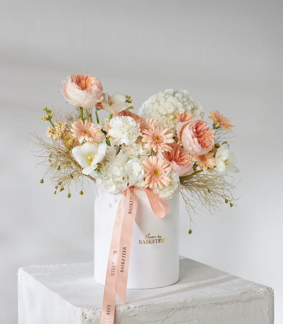 Juliet English garden roses, hydrangeas, and peach gerberas in white cylindrical vase with dried grasses