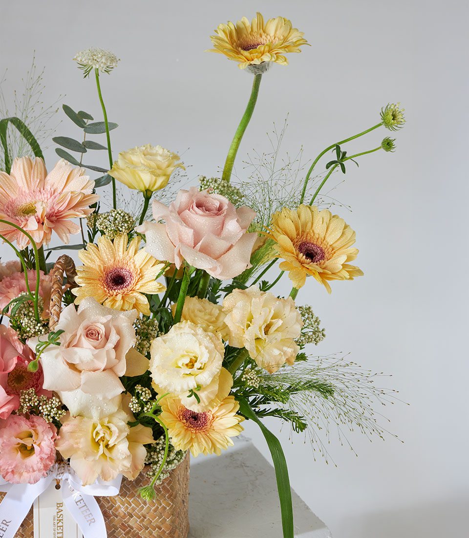 Pastel pink, yellow, and peach roses with gerbera daisies in woven basket, birthday flower gift