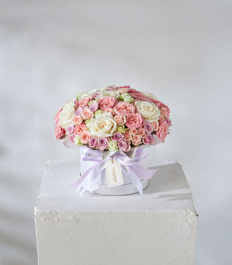 Luxury white hatbox filled with white, pink, lavender, and pale green roses with purple ribbon bow