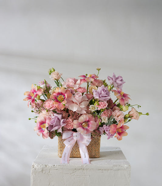 Pastel pink and purple roses with tulips and lilies in woven basket with satin ribbon