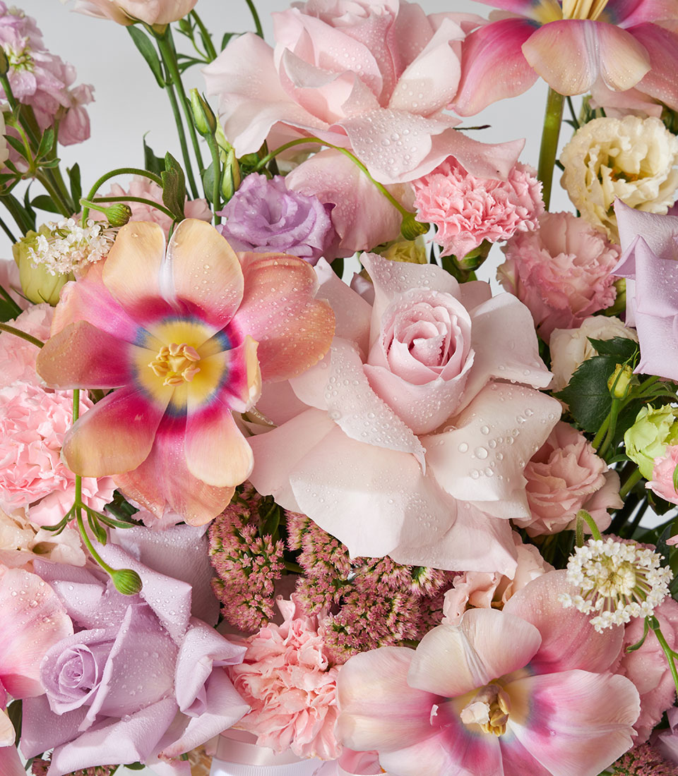 Pink and purple roses, tulips, and carnations in a pastel garden-style basket arrangement