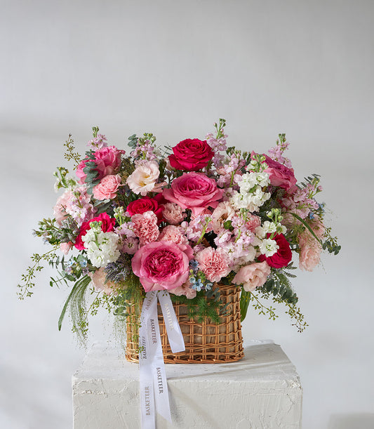Lush pink and white rose garden basket with carnations, stock flowers, and foliage in woven wicker
