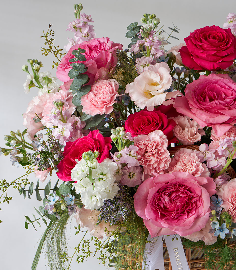 Pink and fuchsia rose garden basket with carnations, stock flowers, and eucalyptus foliage in woven basket