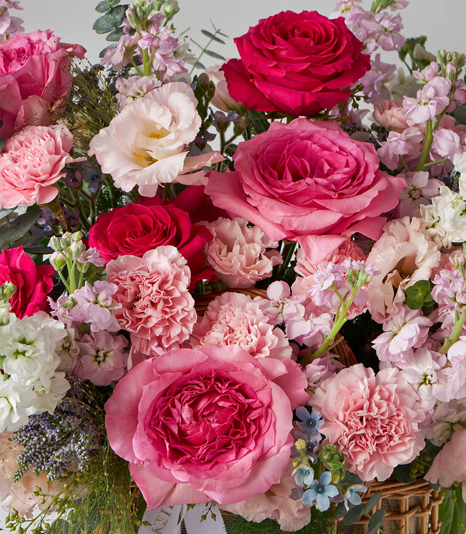 Pink and white roses with carnations, lisianthus, and stock in a woven garden basket with eucalyptus greenery