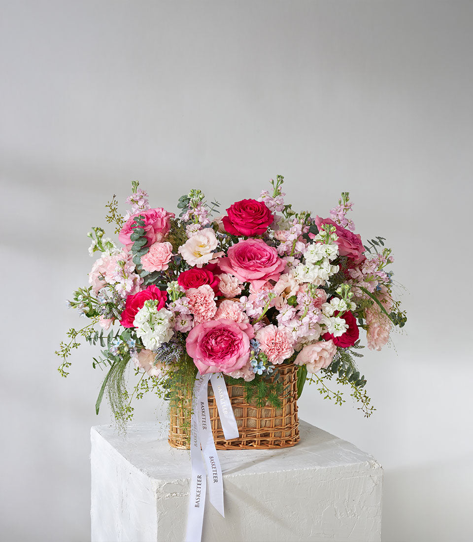 Lush pink and red roses garden basket with white ribbon, premium fresh flower arrangement in woven wicker