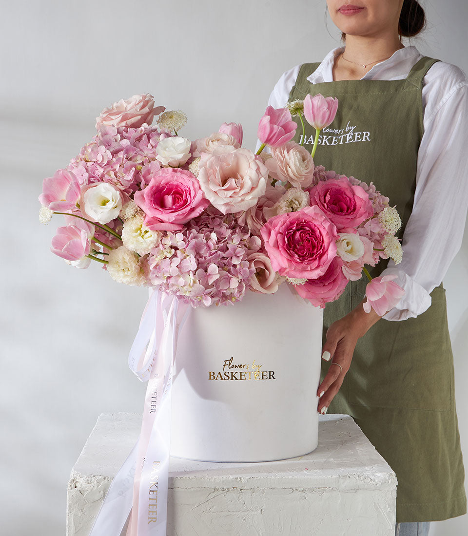 Pink and white roses, ranunculus, and tulips in pearl leather hatbox with Basketeer ribbon