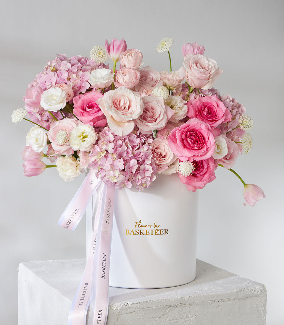 Pink and white roses, ranunculus, and tulips in pearl leather flower box with Basketeer ribbons