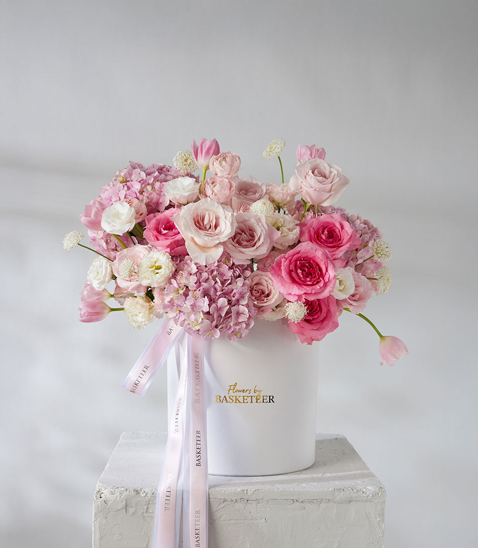 Pink and white roses, ranunculus and tulips in pearl leather hatbox with cascading ribbons