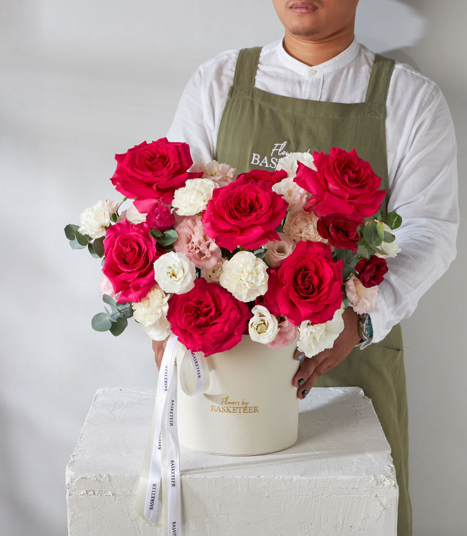 Premium red roses and white lisianthus in cream hatbox with gold branding and ribbon
