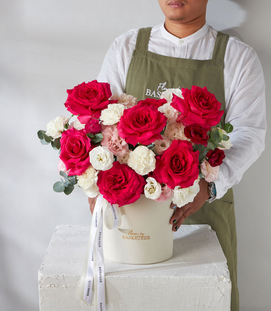 Premium red roses and white lisianthus in cream hatbox with gold branding and ribbon