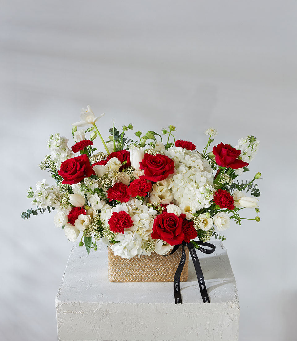 Red roses and white hydrangea arrangement in woven basket with black ribbon bow