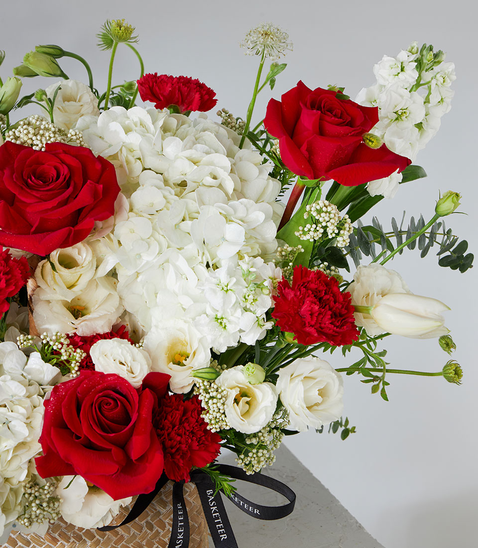Red roses and white hydrangea fresh flower arrangement in woven basket with eucalyptus greenery