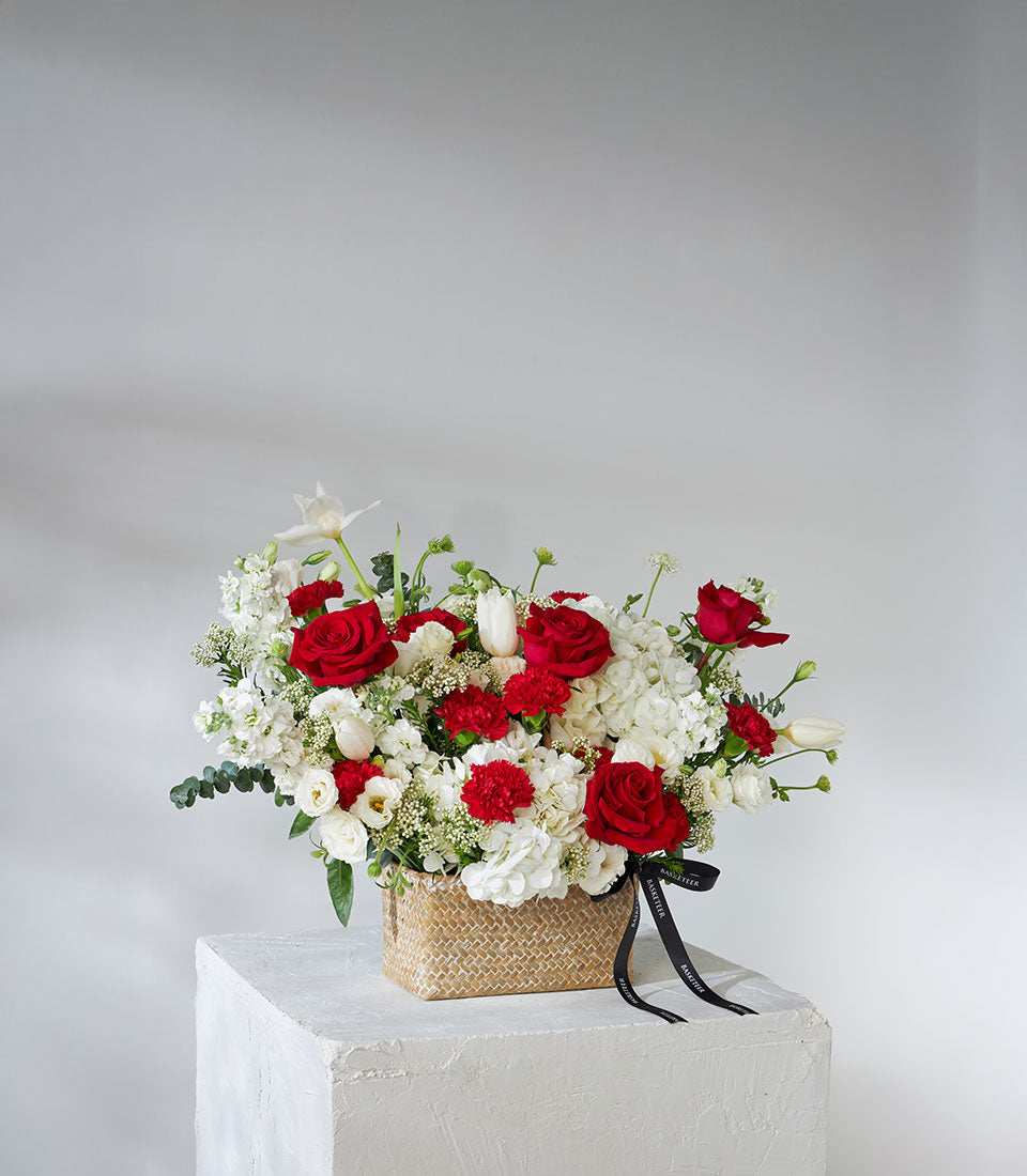 Red roses and white hydrangea arrangement in woven basket with eucalyptus and filler flowers