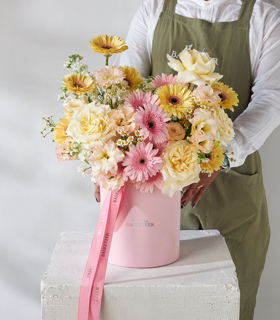 Pink velvet box arrangement with yellow and pink roses, gerberas, and white fillers