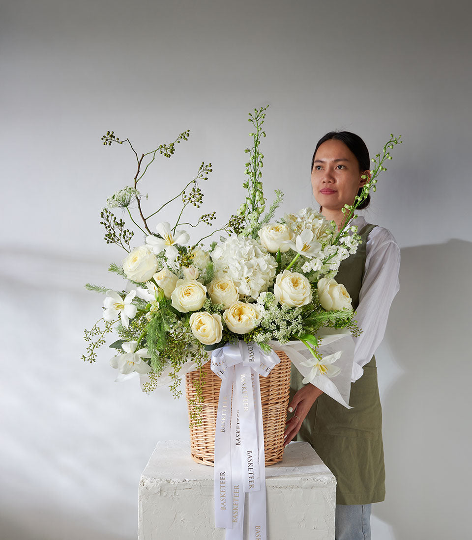 Premium white roses and hydrangea arrangement in woven basket with fresh green foliage