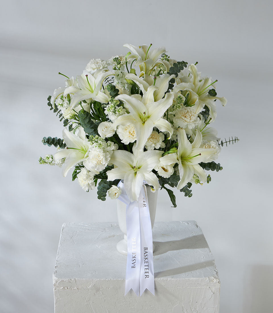 White lilies and carnations in elegant white vase with eucalyptus greenery, premium fresh flower gift arrangement