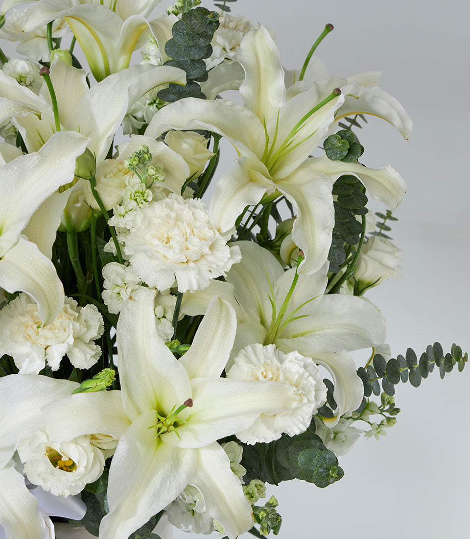 Elegant white lilies and carnations arranged in white vase with eucalyptus greenery