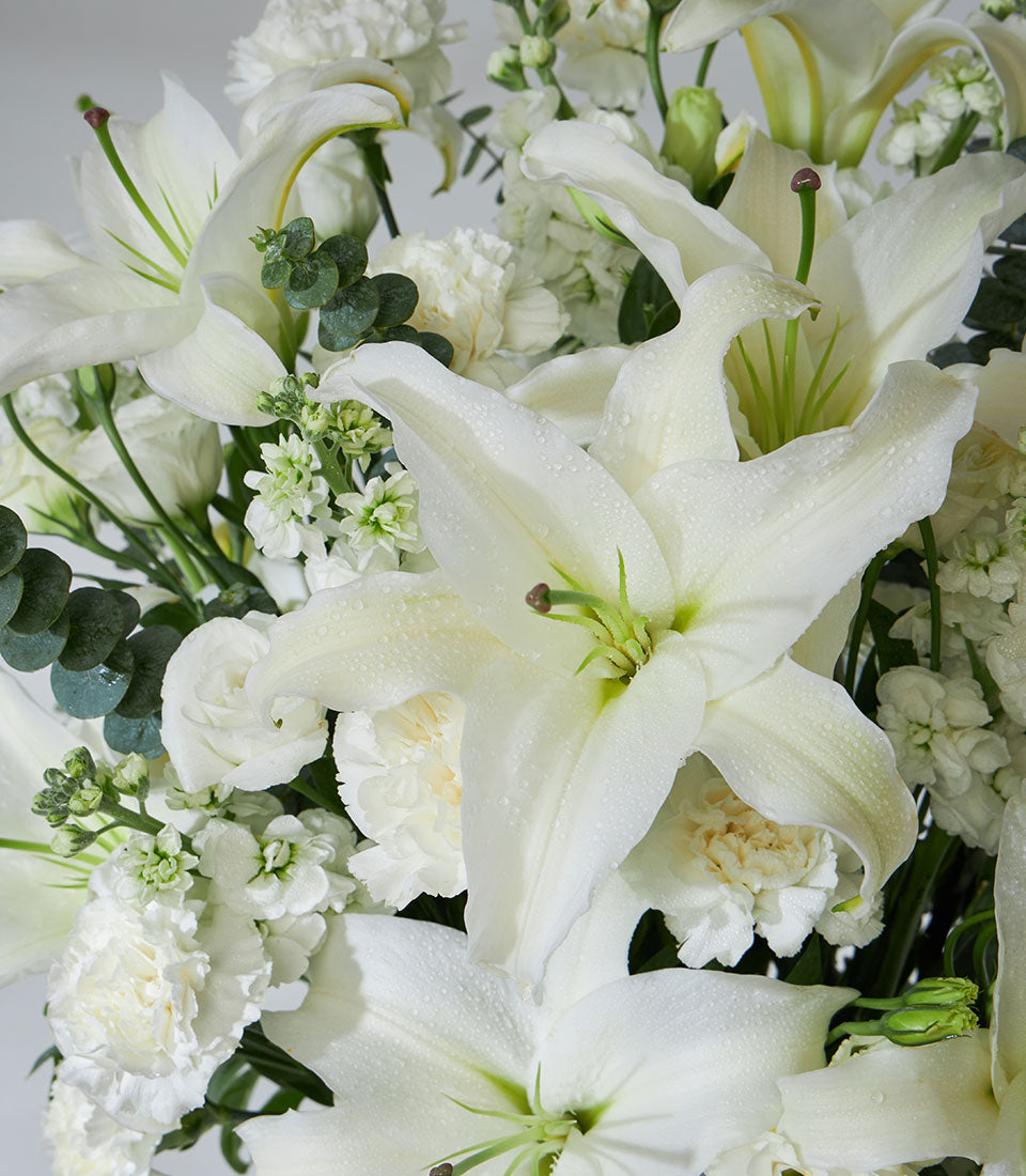 White lilies and carnations fresh arrangement in elegant vase with eucalyptus greenery